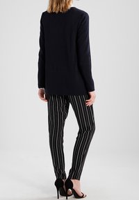 Marinblå lång cardigan, ribbad textur, parat med svarta randiga byxor, figurnära stil, och öppna svarta klackar.