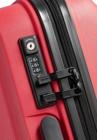 Maleta rígida roja con acabado texturizado, que presenta una cerradura combinada, cremallera negra y el logo de Delsey en los herrajes.