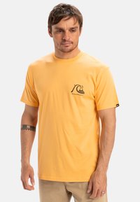 Yellow cotton t-shirt featuring a circular graphic with a wave and mountain design on the left chest. Short sleeves and classic fit.