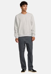 Sweatshirt gris en tissu doux, doté d'un col rond et de poignets côtelés, associé à un pantalon gris foncé et des baskets noires.