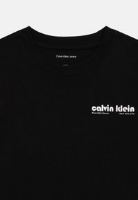 Černé bavlněné tričko s kulatým výstřihem. Na levé hrudi se nachází bílé logo, které uvádí "Calvin Klein" a "West 39th Street, New York City."