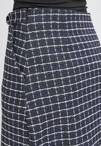 Jupe texturée bleu marine avec motif à carreaux blancs et détail boutons noirs portée avec un haut noir.