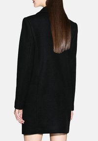 Abrigo negro de lana con silueta entallada, solapas con muesca y mangas largas, con un acabado limpio y largo hasta la mitad del muslo.