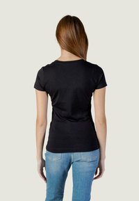 Schwarzes Kurzarm-T-Shirt mit Rundhalsausschnitt, körperbetontem Design und glatter Baumwollstruktur, von hinten gezeigt. Hellblaue Jeans sichtbar.