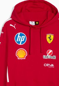 Sarkana kapuce ar auklu, rotāta ar logotipiem: HP (zils aplis), Shell, UniCredit un Ceva Logistics. Balti akcenti uz piedurknēm.