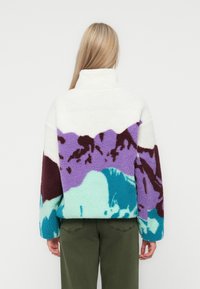 Pullover in pile con colletto alto e un motivo multicolore di montagne in viola, verde acqua e bianco. Maniche lunghe con polsini elasticizzati.