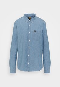 Camicia in denim azzurro chiaro a maniche lunghe con colletto button-down, taschino sul petto e bottoni bianchi. Presenta un'etichetta con logo nero sulla tasca.