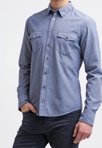 Dark blue button-up shirt with a subtle texture, featuring two chest pockets, metal buttons, and a pointed collar. Long sleeves, straight hem.