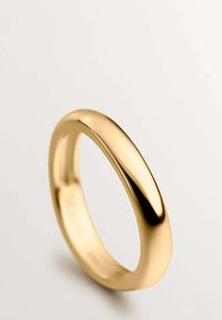 Anillo de metal dorado con una superficie lisa y pulida, forma redondeada y sin adornos visibles. Diseño simple y minimalista.