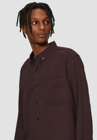 Chemise boutonnée bordeaux avec col, poche poitrine unique et tissu texturé. Caractéristiques : coupe décontractée et boutons contrastants.