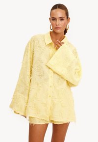 Gele gestructureerde shirt met kraag, oversized pasvorm en lange mouwen. De stof heeft een zachte, rafelige uitstraling en voorste knopen.