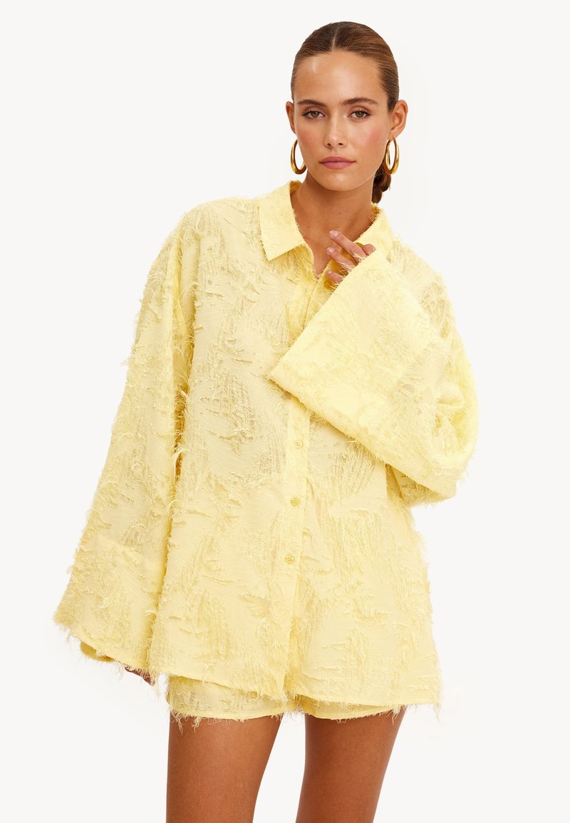 Gele gestructureerde shirt met kraag, oversized pasvorm en lange mouwen. De stof heeft een zachte, rafelige uitstraling en voorste knopen.