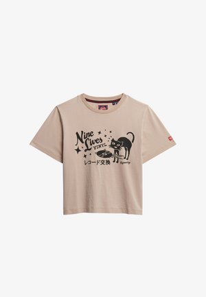 Camiseta de algodón color beige claro con un gráfico negro de un gato con un disco de vinilo y el texto "Nine Lives VINYL" rodeado de estrellas.