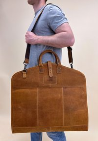 Braune Ledertasche mit strukturiertem Design, oberen Griffen und verstellbarem Riemen. Mit Steppdetails und einem Markenpatch.