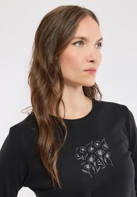 Chemise à manches longues noire ornée de broderies florales blanches sur le devant. Tissu doux avec un col rond et un design ajusté.