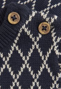Marinblå stickad tröja med en diamantmönster i krämfärg, ribbad krage och två runda, ljusbruna knappar på axeln.