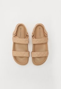 Beige vegan leren sandalen met gestikte banden, verstelbare gespen en een platte zool. Ontworpen voor comfort en casual gebruik.