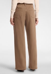 Pantalones de pierna ancha en una tela marrón clara, con una cintura alta, bolsillos traseros y una textura suave con un acabado limpio en los dobladillos.