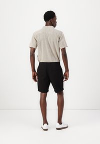 Kortärmad mönstrad skjorta i beige och brunt, kombinerad med svarta shorts. Modellen har på sig vita sneakers. Släta tyger och avslappnad passform.