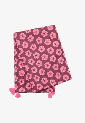 Tissu violet plié avec des motifs de fleurs d'hibiscus roses et des pampilles roses aux coins.