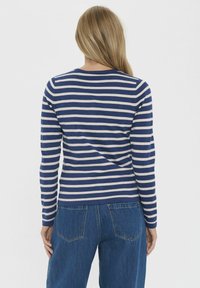 Camisa de manga larga a rayas en azul marino y beige con cuello redondo, combinada con vaqueros de mezclilla azules que tienen dos bolsillos en la parte posterior.