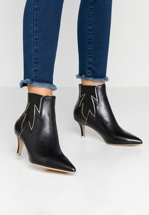 Sort ankelhøje læderstøvler med hæl, spidse tåpartier og zigzag-sømme, båret med blå jeans med frynset kant.