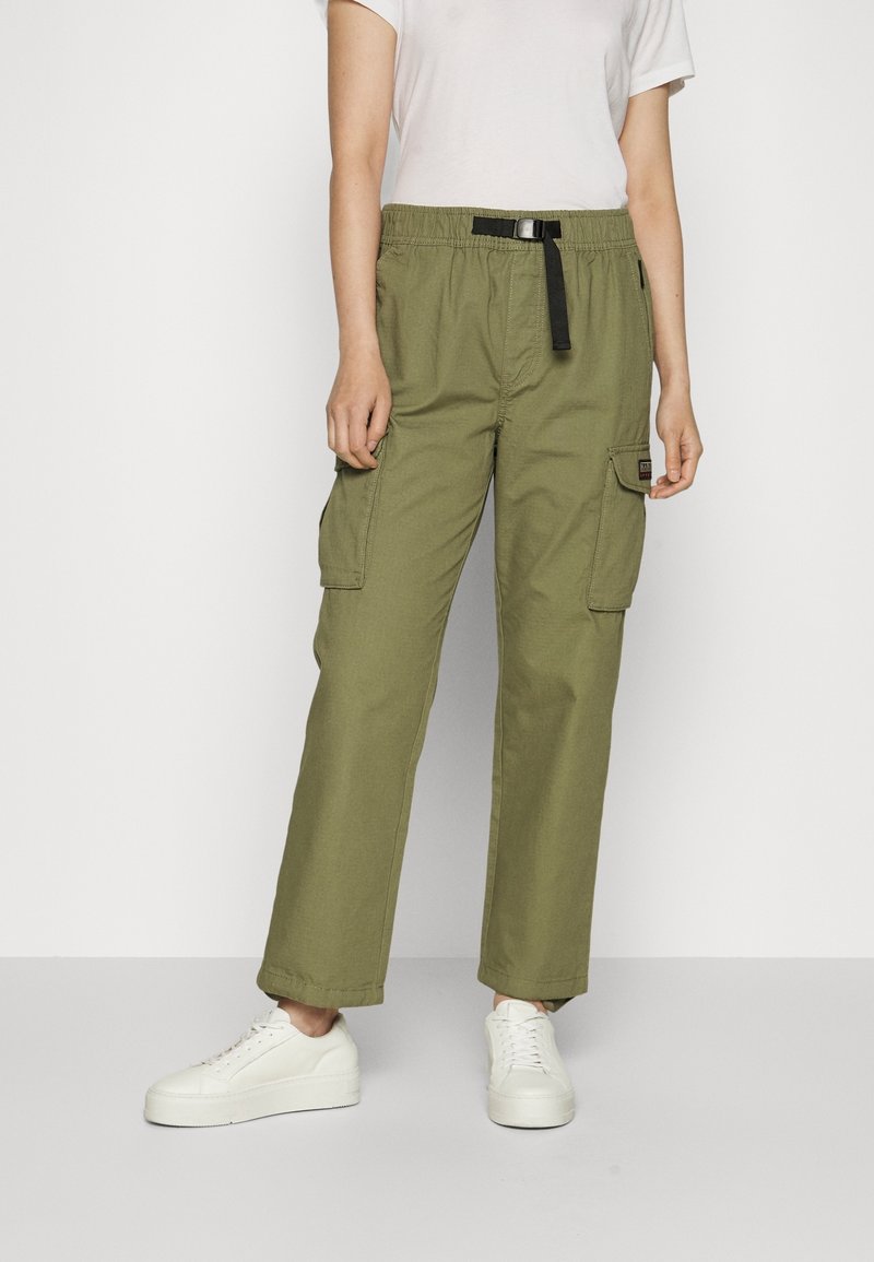 Olijfgroene cargobroek met een elastische tailleband, zwarte trekkoord, zijzakken en een relaxte pasvorm. G gedragen met witte sneakers.