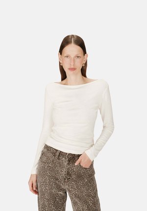 Haut à manches longues de couleur blanc cassé, fait de matériel doux, avec un décolleté bateau. Associé à un jean taille haute à imprimé léopard pour créer un contraste.
