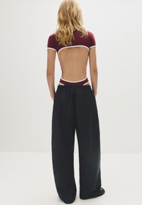 Bordeaux bodysuit met ruguitsnijding en witte bies, gecombineerd met zwarte broeken met wijde pijpen. Gladde textuur, losse pasvorm, casual ontwerp.