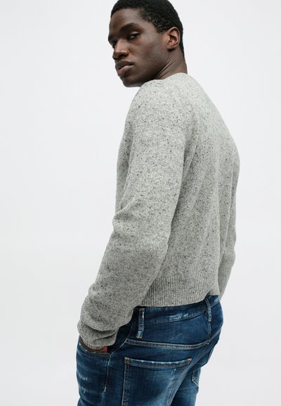Lichtgrijze gebreide trui met een gespikkeld textuur, ronde halslijn en geribbelde manchetten, gecombineerd met donkerblauwe versleten jeans.