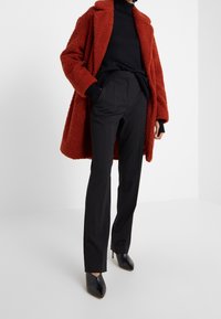Rode fluffige jas met een kraag, gedragen over een zwarte coltrui, gecombineerd met zwarte op maat gemaakte broeken en zwarte spitse hakken. Eenvoudig ontwerp.