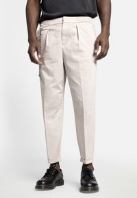 Lys beige tapered bukser med læg, elastisk talje og sølv kædedetalje. Båndet med sorte snørebåndssko.
