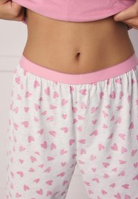 Roze pyjamashorts met een elastische tailleband, voorzien van een witte stof versierd met kleine roze hartpatronen. Zachte textuur.
