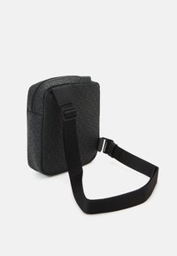 Borsa a tracolla nera con un motivo geometrico, forma rettangolare, lati imbottiti, tracolla regolabile e una superficie liscia.