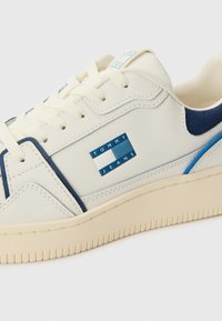 Baskets blanches et marines avec un design texturé, semelle en caoutchouc, lacets et un détail logo bleu "TOMMY JEANS" sur le côté.