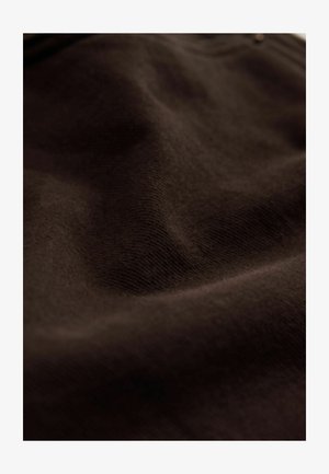 Brauner Stoff mit einer weichen Textur, der eine subtile Dehnbarkeit und eine glatte Oberfläche aufweist und natürliche Falten und Wellen zeigt.