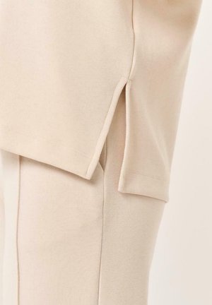 Top in misto cotone beige con spacco laterale e maniche corte, caratterizzato da una vestibilità morbida e una texture liscia.