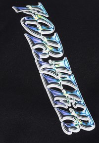 Black fabric featuring raised, iridescent lettering with curved shapes and sharp accents, creating a bold visual effect.