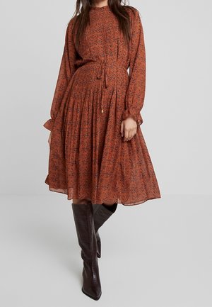 Mujer con vestido midi estampado floral color óxido, mangas largas y cintura atada, combinado con botas altas marrón oscuro.
