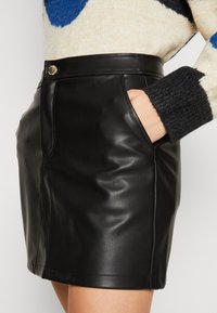 Schwarzer Leder-Minirock mit Fronttaschen und taillierter Passform. Mit metallischem Knopfverschluss an der Taille und glatter Textur.