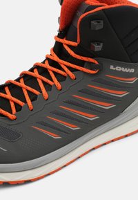 Schwarzer und grauer Wanderschuh mit orangefarbenen Akzenten, ausgestattet mit einem strukturierten Obermaterial, leichtem Design und Gummisohle. Reflektierende Details sind vorhanden.