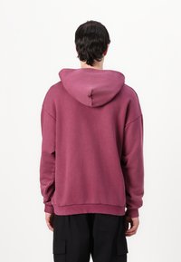 Felpa con cappuccio color marrone scuro, dal taglio rilassato, con polsini e orlo a costine, realizzata in morbido cotone, senza motivi visibili.