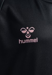 Czarna tkanina o gładkiej fakturze z różowym logo stylizowanej pszczoły oraz słowem "hummel" poniżej.