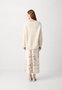 Suéter crema acogedor con una textura suave, combinado con una falda de tonos pastel y estampado floral. El conjunto cuenta con un corte holgado y mangas largas.
