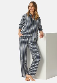 Marineblauw en witte gestreepte pyjama set gemaakt van een gladde stof. Bevat een overhemd met knopen en lange mouwen, evenals een broek met een relaxte pasvorm.
