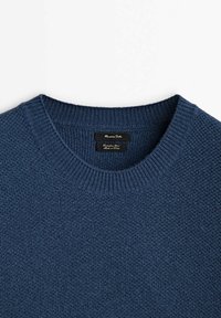 Pull en maille bleu marine avec col rond, présentant un motif texturé et des poignets côtelés. Étiquette noire visible au niveau du col.
