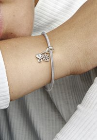 Strieborný náramok s príveskami so štruktúrovaným pásom a tromi dekoratívnymi príveskami: srdcom, symbolom nekonečna a detailným kľúčom.