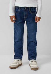 Tmavě modré denimové džíny s pěti kapsami, rovným střihem, prošíváním a knoflíkovým zapínáním. Vybaveno bílými teniskami.