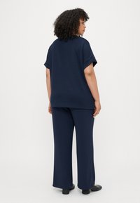 Ναυτικό μπλε, ελαφρώς φαρδύ τοπ με κοντά μανίκια που κυλούν, συνδυασμένο με παντελόνι με φαρδιά πόδια που ταιριάζει. Μαλακή υφή, μινιμαλιστικός σχεδιασμός και χωρίς ορατά σχέδια.