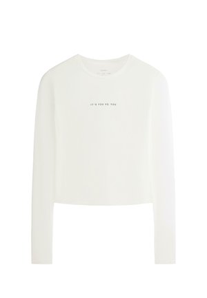 Top scurt alb cu mâneci lungi, gât rotund și text negru "IT'S YOU VS. YOU" centrat pe piept.